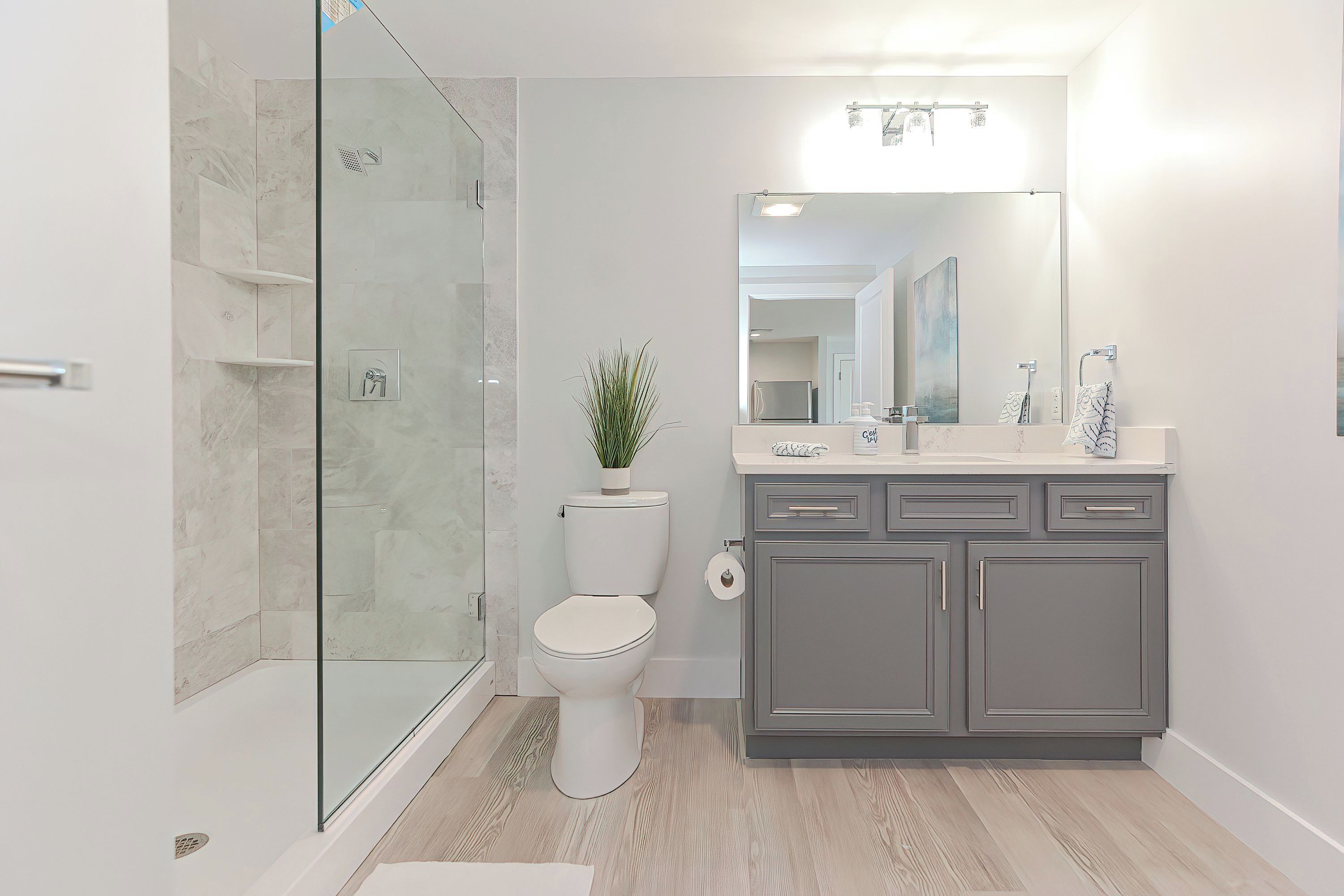 Un baño moderno con cabina de ducha de vidrio, inodoro, lavabo con espejo y una planta en maceta.