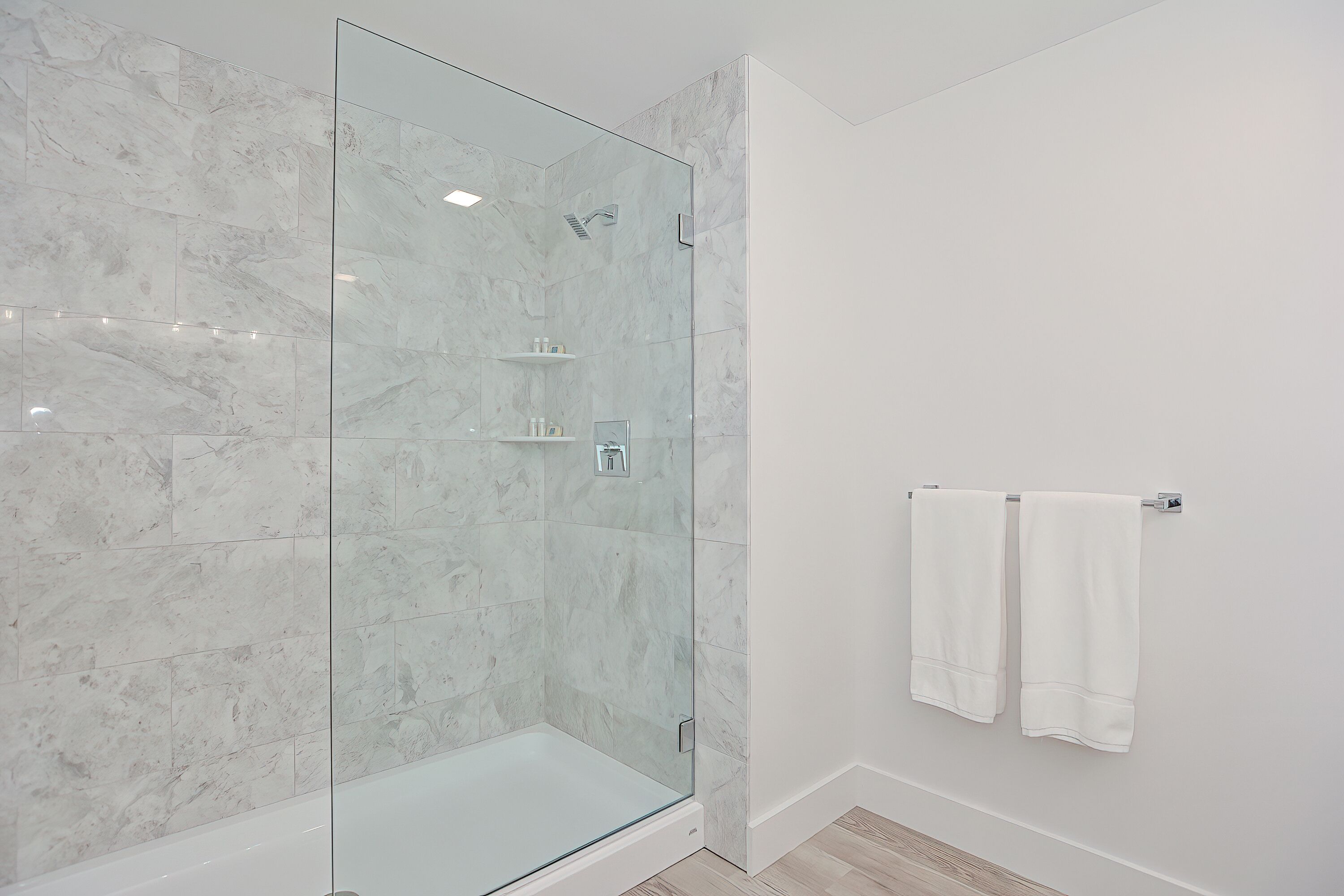 Une salle de bain moderne avec une douche à parois de verre, des carreaux de marbre blanc et un porte-serviettes blanc.