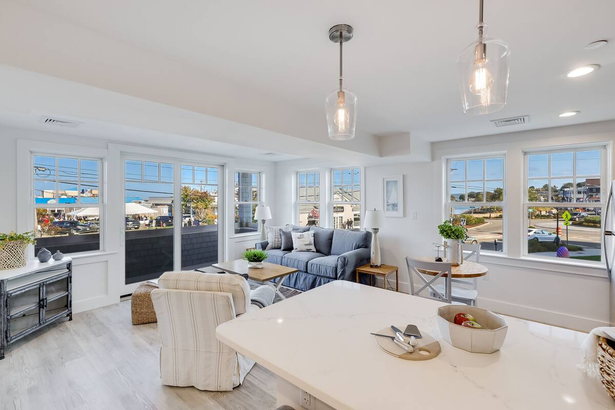 A spacious living room with a large white marble table, a blue sofa, and a view of the street through large windows.