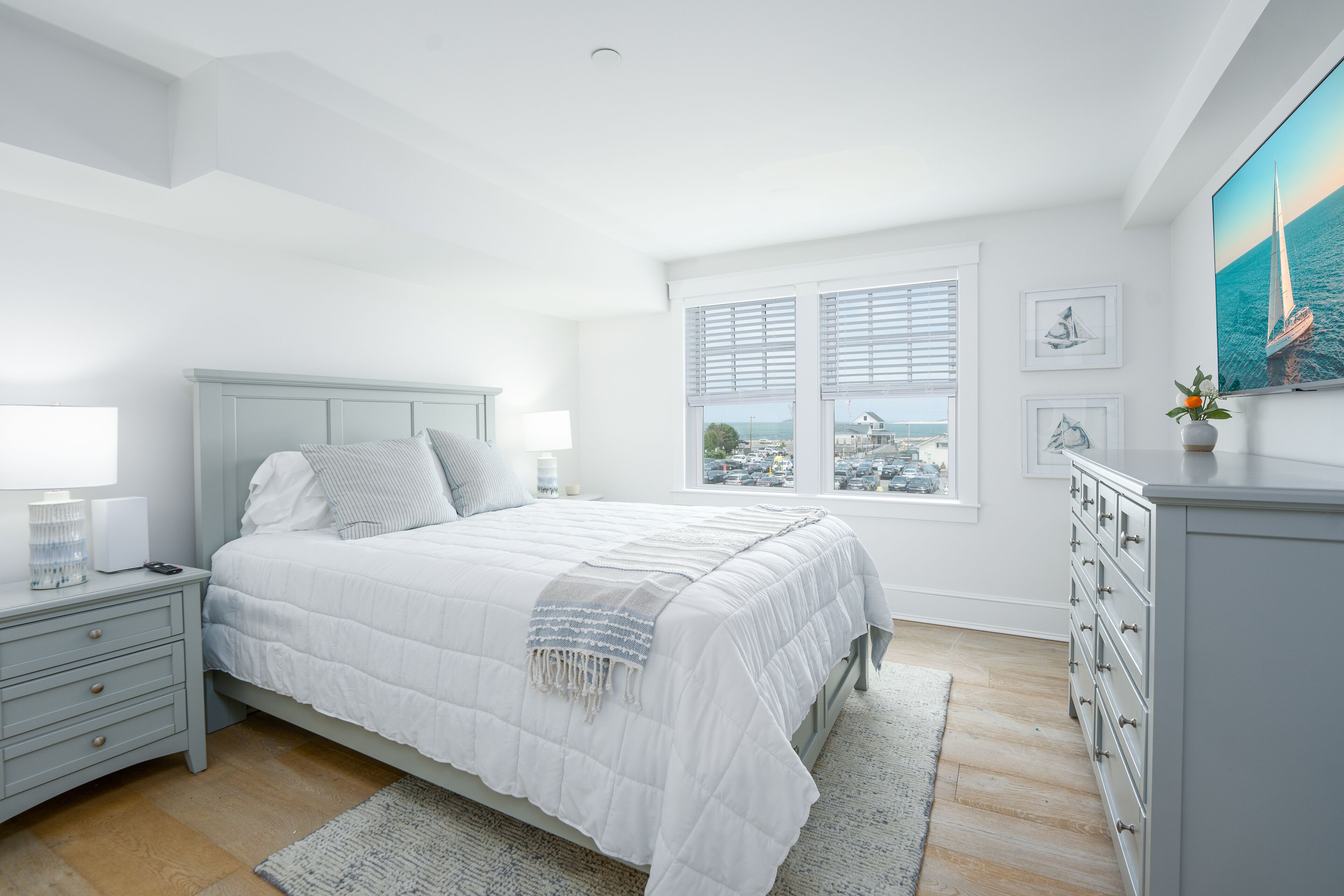 A bedroom with a bed, bedside tables, a dresser, a window with blinds, and a painting on the wall.