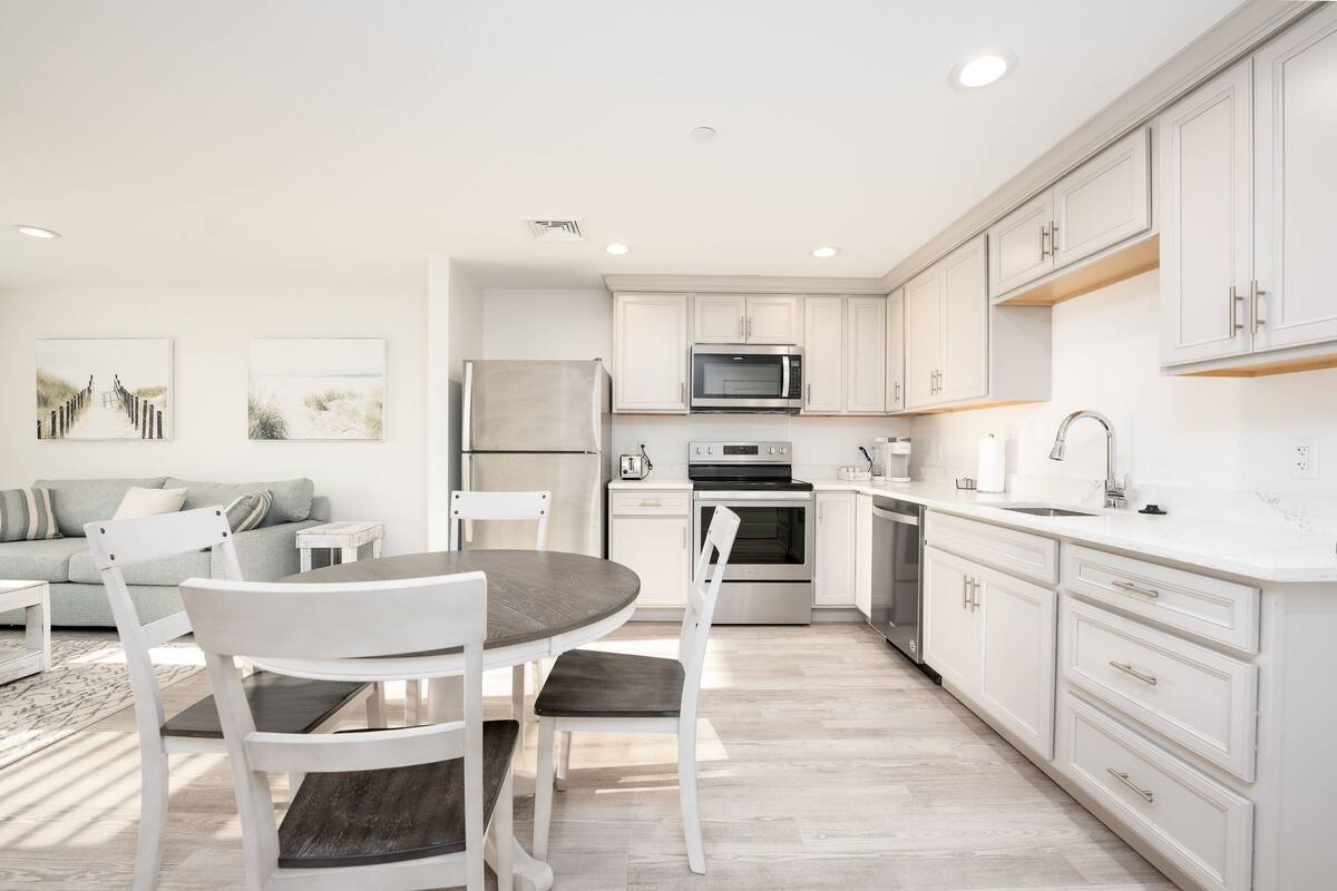 A modern kitchen with white cabinetry, a dining area with a round table and chairs, and a built-in oven.