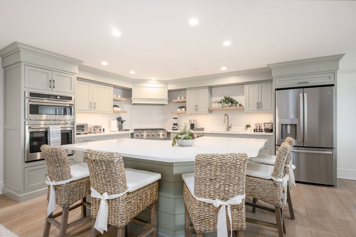 A modern kitchen with a central island, built-in appliances, and wicker chairs.