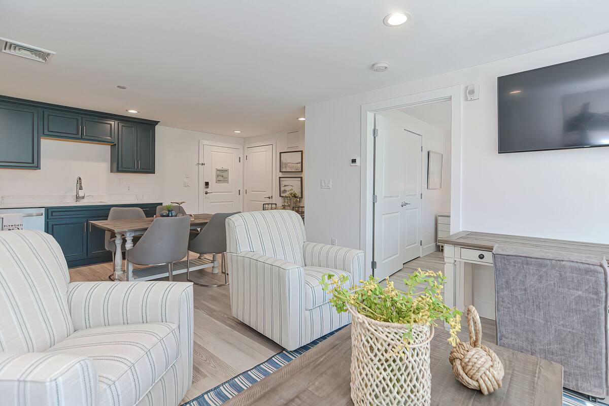 A modern living room with striped sofas, a dining area, and a kitchen with teal cabinets.