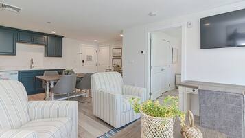A modern living room with striped sofas, a dining area, and a kitchen with teal cabinets.