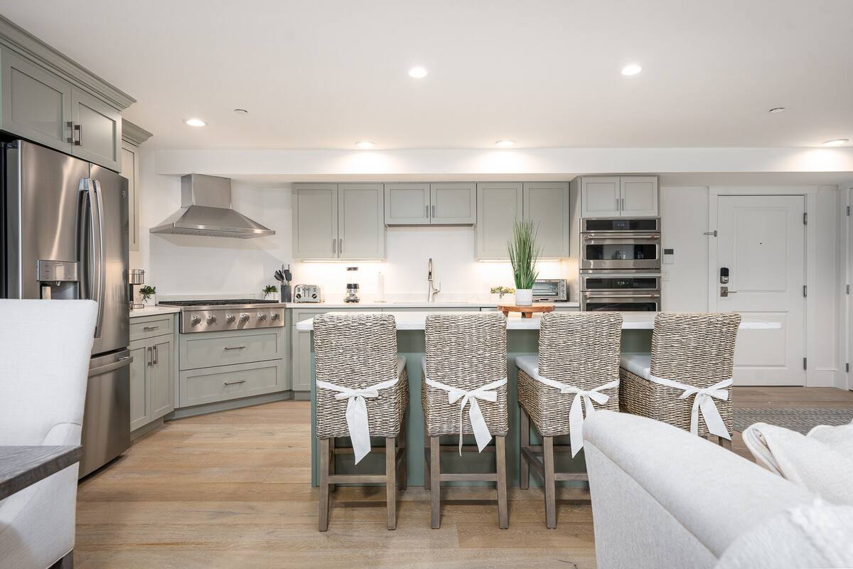 A modern kitchen with stainless steel appliances, light-colored cabinets, and a central island with chairs.