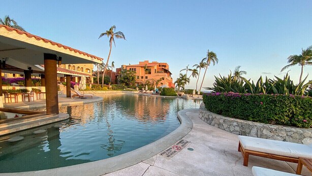 A swimming pool area with lounge chairs, palm trees, and a building in the background. - Beach Front Pool Fully Kitchen Breathtaking Sea Views Close to Everything (San Jose Del Cabo)
