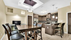 A modern kitchen with a central island, dark wooden chairs, and a ceiling skylight. - Relax & Enjoy In Our Spacious Townhome Getaway! (McAllen)
