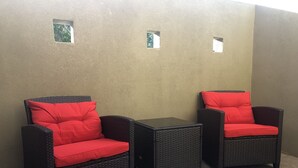 Two wicker chairs with red cushions and a small table, set against a plain wall with two small windows. - Relax & Enjoy In Our Spacious Townhome Getaway! (McAllen)