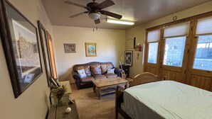 Una habitación acogedora con cama, una mesa de madera, un sofá de cuero y un ventilador de techo.