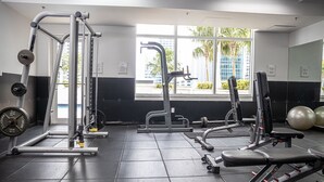 A gym with weightlifting equipment, exercise balls, and a window with a view of palm trees and buildings. - **NEW** Ocean Front 3 Bedroom Apartment in the heart of Brickell (Miami)