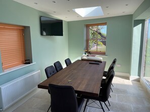 A conference room with a long table, black chairs, a flat-screen TV, a window with blinds, and a skylight.