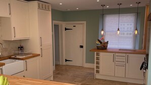 A modern kitchen with wooden countertops, white cabinets, and a built-in oven. There is a window with blinds and pendant lighting.