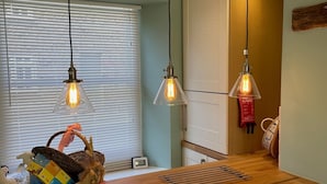 A kitchen with a wooden countertop, three pendant lights, a basket with items, and a window with blinds.