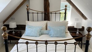 A bedroom with a sloped ceiling, a bed with a metal frame, two bedside tables with lamps, and a large window.
