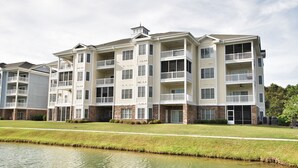 A multi-story residential building with balconies, a flat roof, and a grassy area in front. - Lake & Pool View in the Heart of Myrtle Beach, SC-Magnolia Pointe-Myrtlewood (Myrtle Beach)