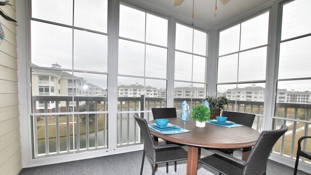 A covered patio with a round table, four wicker chairs, a blue bowl, a potted plant, and a blue placemat. - Lake & Pool View in the Heart of Myrtle Beach, SC-Magnolia Pointe-Myrtlewood (Myrtle Beach)