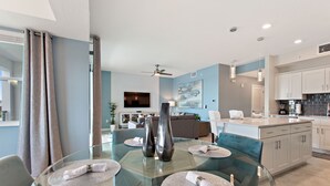 A modern dining area with a glass table, two vases, and a blue sofa in the background. - Water View, Pool Table, Resort Amenities Included! (Kissimmee)