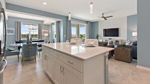 A modern kitchen with a central island, dining area with chairs, and a living room with a sofa and TV. - Water View, Pool Table, Resort Amenities Included! (Kissimmee)
