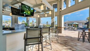 An outdoor bar area with high ceilings, large windows, and a TV screen displaying a nature scene. - Water View, Pool Table, Resort Amenities Included! (Kissimmee)