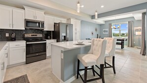A modern kitchen with white cabinetry, a central island, and a dining area with a view. - Water View, Pool Table, Resort Amenities Included! (Kissimmee)