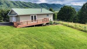 Una casa de un piso con techo verde, una terraza de madera y un patio cercado.