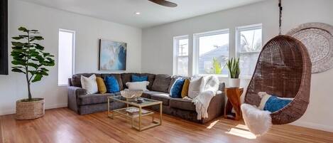 Un salon moderne avec un canapé gris, un fauteuil suspendu, une table basse et un ventilateur de plafond.