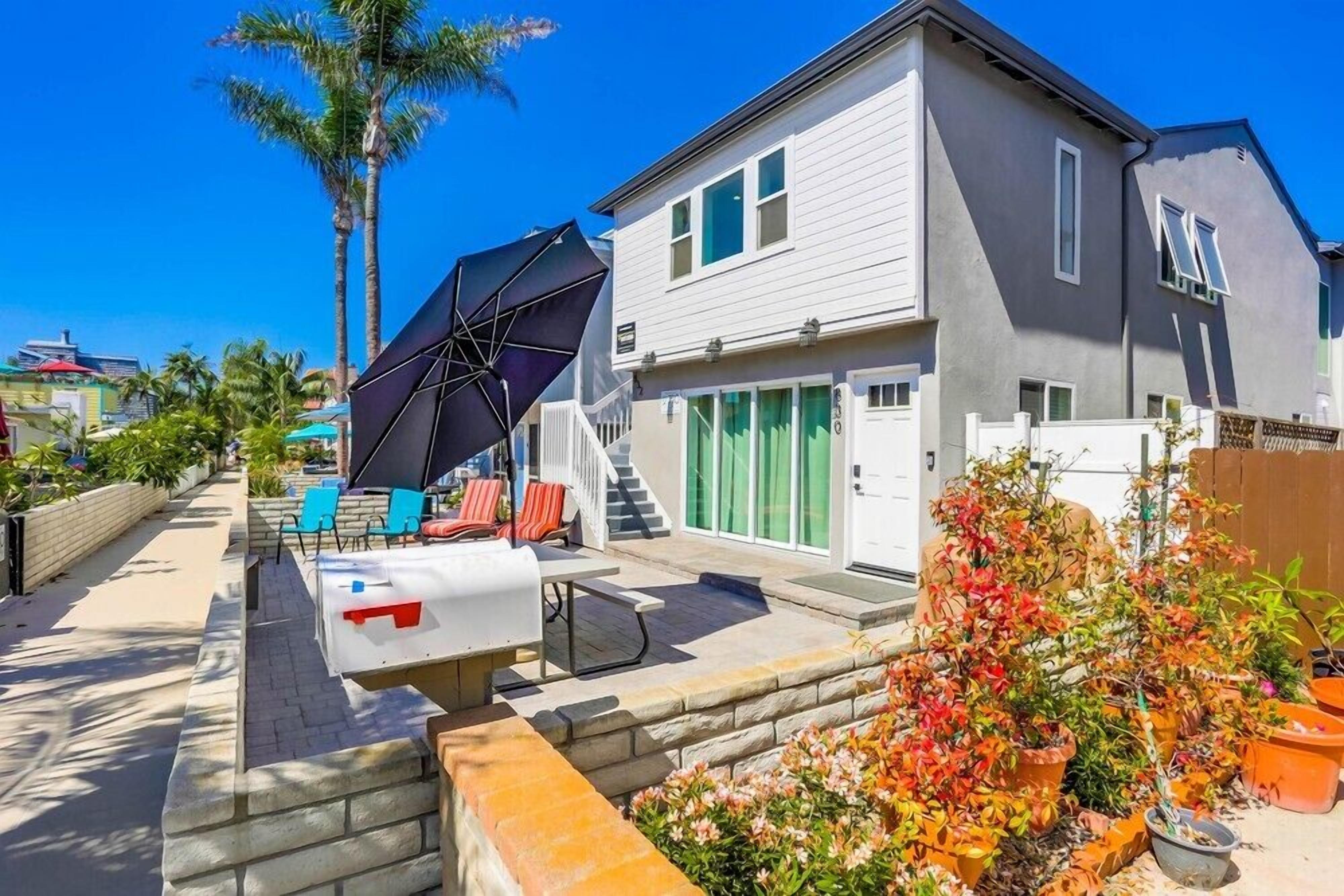Une maison à deux étages dotée d’un patio aménagé avec du mobilier d’extérieur et un grand parasol.