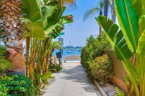 A pathway leading to a beach with boats in the water, surrounded by lush tropical plants.