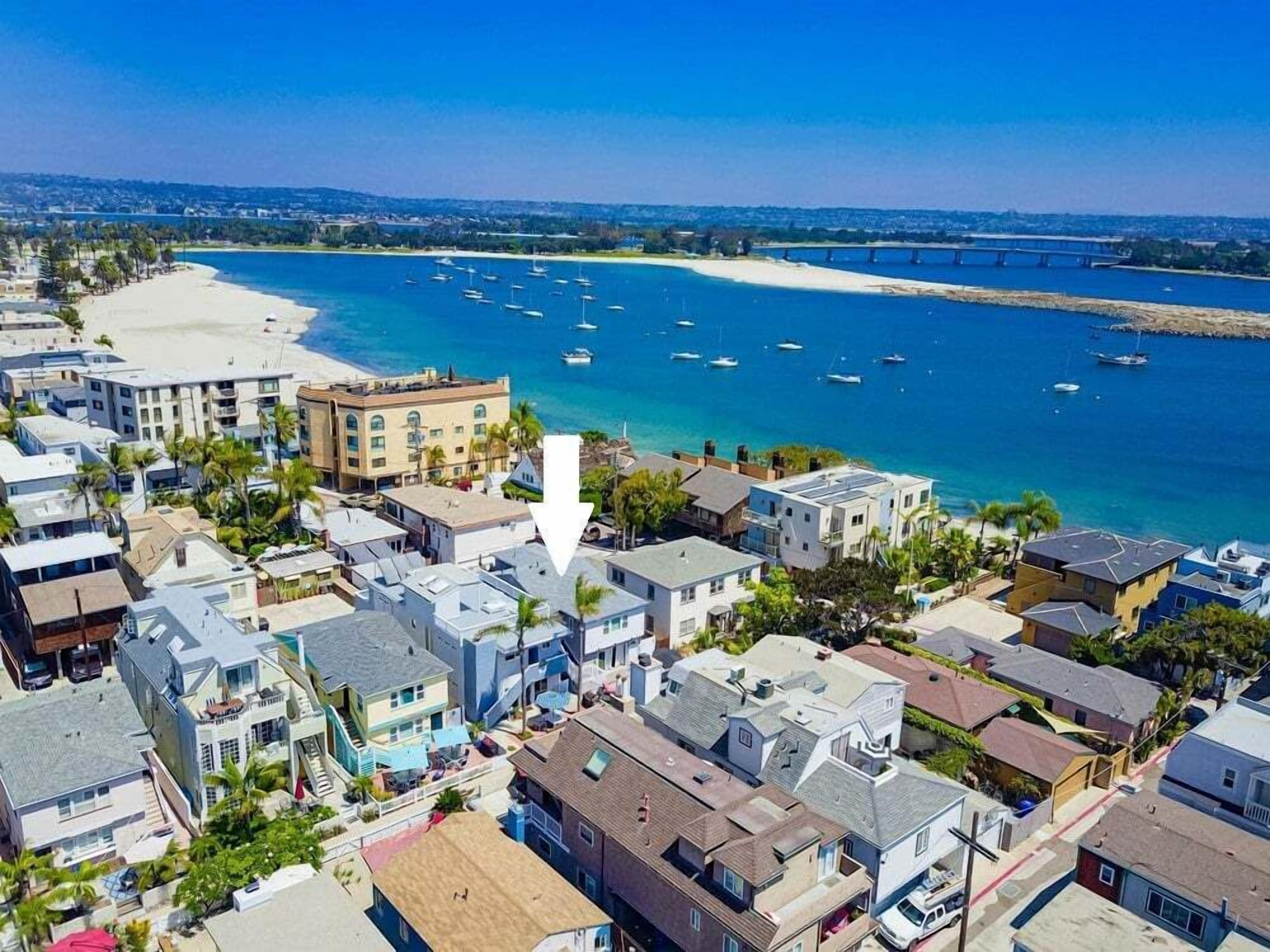 Una zona residencial costera con propiedades frente a la playa, una playa de arena y barcos en el agua.