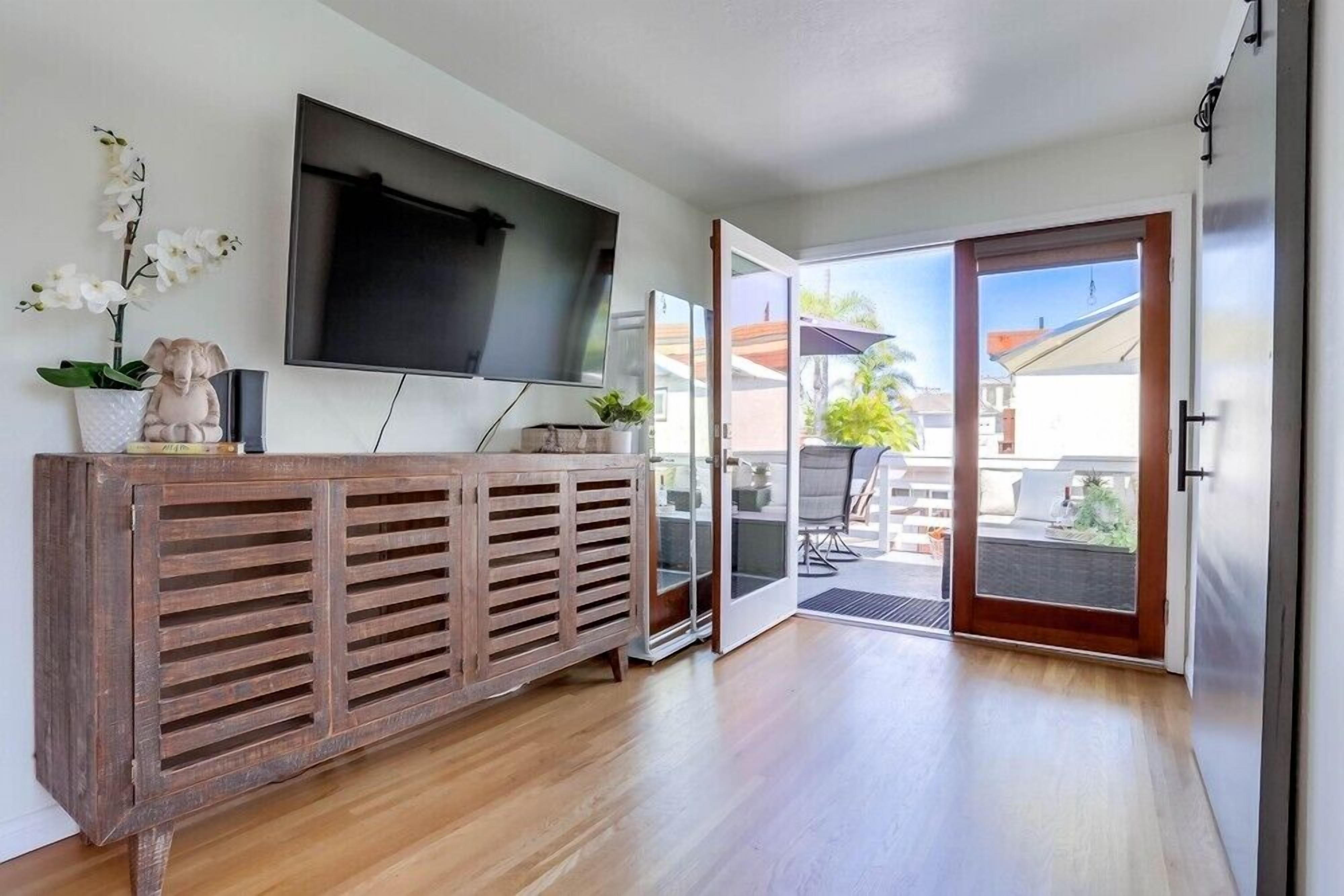 Una sala de estar moderna con una consola de madera, un televisor de pantalla plana y un ventanal corredero que da a un espacio exterior.