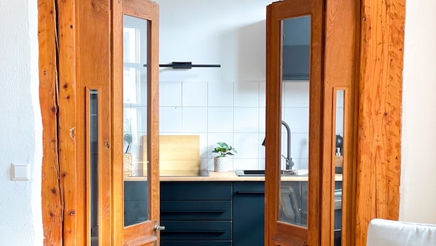 A wooden-framed doorway leading to a kitchen with a sink, cabinets, and a small plant.