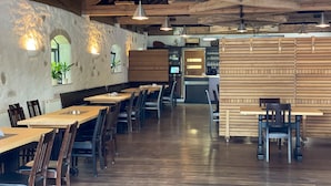 A restaurant with wooden tables and chairs, a counter, and a stone wall with arched windows.