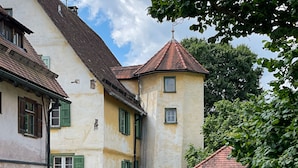 A traditional building with a steeply pitched roof, a small tower, and a well-maintained garden.