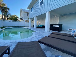 A pool area with lounge chairs, a covered patio, and a white fence.