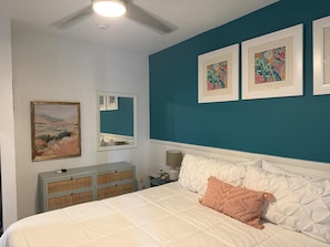 Une chambre à coucher comprenant un lit, une commode, un miroir et deux œuvres d’art encadrées accrochées au mur.