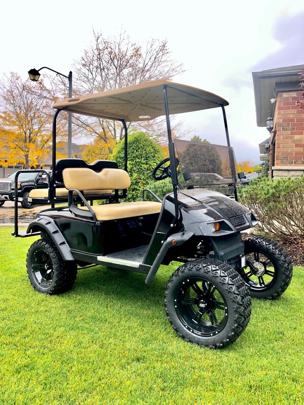 A golf cart parked on a grassy area with a brick building in the background.