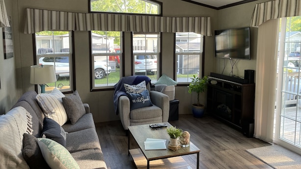 Un salon chaleureux avec un canapé, un fauteuil, une table basse et une cheminée. De grandes fenêtres offrent une vue sur l’extérieur.