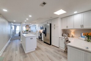 Une cuisine moderne avec des meubles blancs, un îlot central et un réfrigérateur en acier inoxydable.