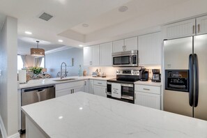 A modern kitchen with white cabinetry, stainless steel appliances, and a marble countertop. - Aqua Blu at Anna Maria Island Club 27 (Bradenton Beach)