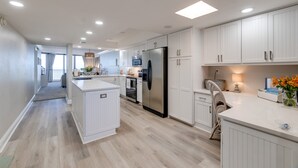 Una cocina moderna con muebles blancos, una isla central, electrodomésticos de acero inoxidable e iluminación empotrada.