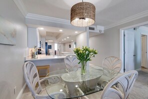 Un coin repas avec une table ronde en verre, entourée de chaises en osier, un luminaire suspendu et un vase rempli de fleurs.