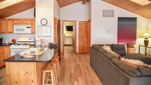 A spacious kitchen with wooden cabinets, a central island with stools, and a dining area with a sofa and lamp. - 3 bedroom accommodation in Red River (Red River)