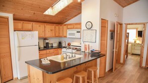 A kitchen with wooden cabinets, a central island with stools, a refrigerator, a microwave, and a sink. - 3 bedroom accommodation in Red River (Red River)