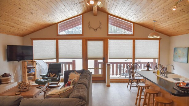 A spacious living area with a high ceiling, a large sofa, a dining table with chairs, and a kitchen area with stools. - 3 bedroom accommodation in Red River (Red River)