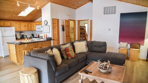 A modern living space with a large sectional sofa, wooden flooring, a kitchen area, and a large abstract painting on the wall. - 3 bedroom accommodation in Red River (Red River)