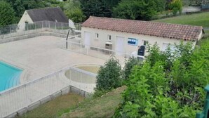 Una propiedad residencial con piscina, un patio cercado y una casa con techo de tejas rojas.