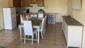 Cocina compacta con armarios de madera, un refrigerador blanco, una mesa de comedor con sillas y una pequeña encimera con un lavamanos.
