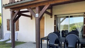 Un patio techado al aire libre con una mesa y sillas, una pérgola de madera y un ventanal que da a un balcón.