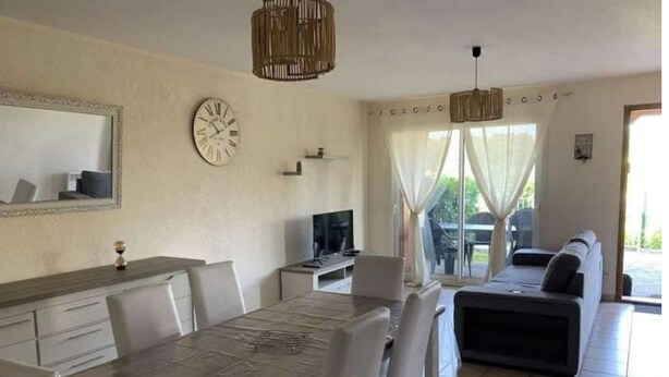 Una sala de estar moderna con comedor, un sofá, un televisor y un amplio ventanal con cortinas.