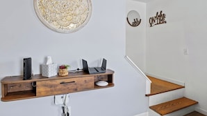 A modern home office with a wooden desk, two laptops, a book, a tissue box, and a decorative wall piece.